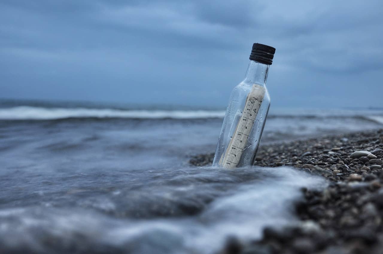 Papel enrolado dentro de uma garrafa de vidro na areia da praia